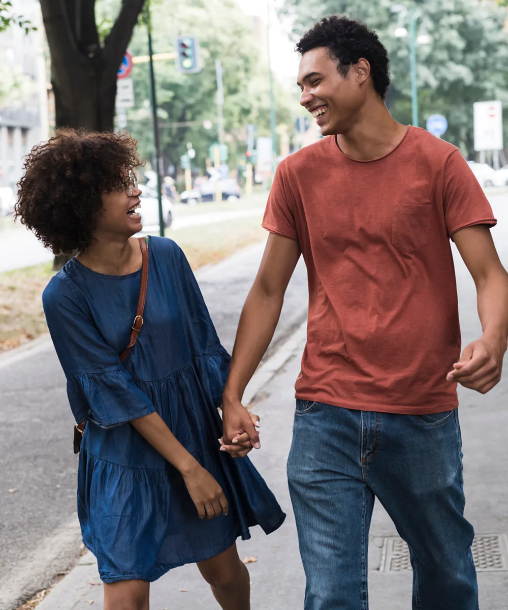 Young black couple laughing as they walk holding hands.