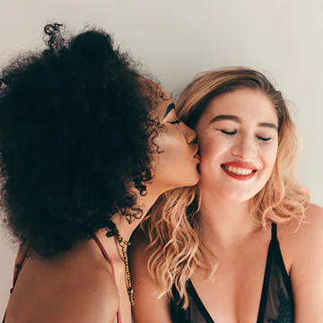 Young woman kissing her girlfriend’s cheek.