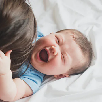 Baby laughing as someone tickles his tummy.