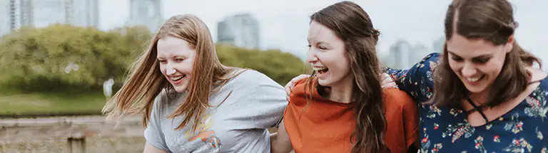 Three young women laughing as they walking holding each other.