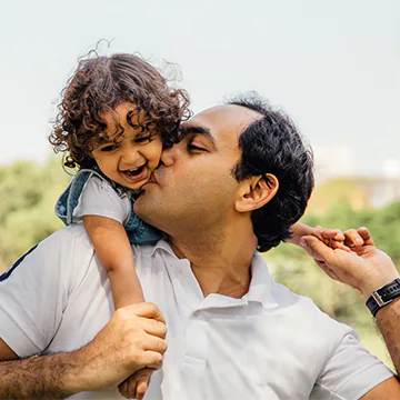 Father holding his young daughter on his back and kissing her cheek.